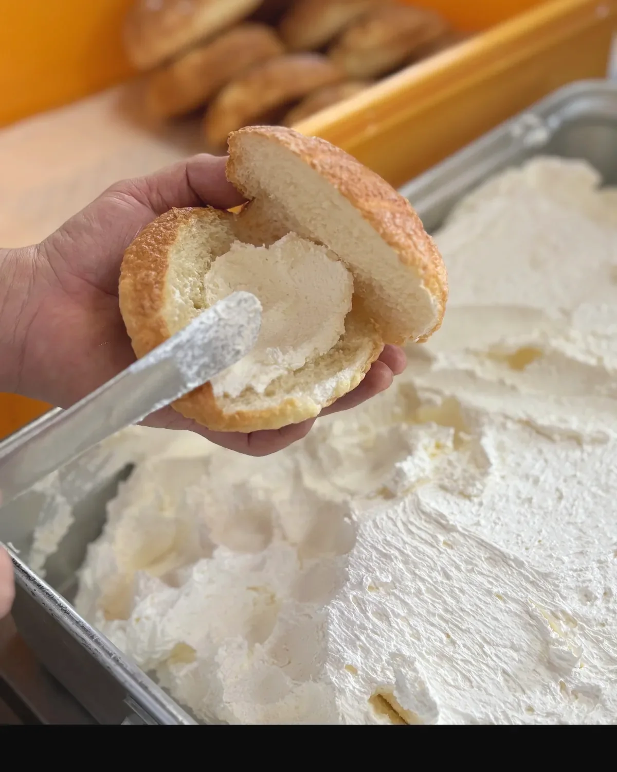割ったメロンパンに、手作りのバタークリームをへらで塗っているところ