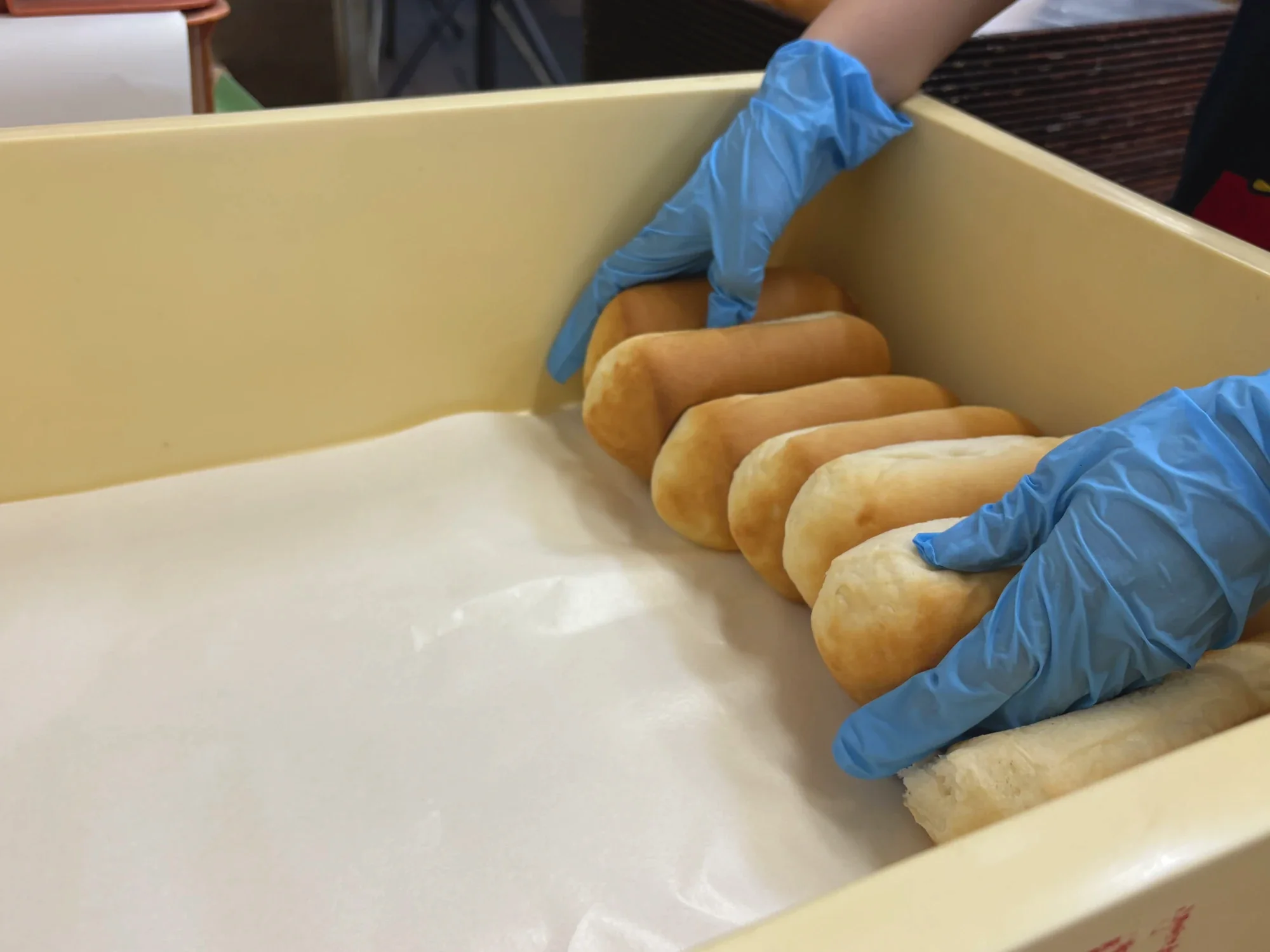 青い手袋で給食用のパンを箱に並べる作業